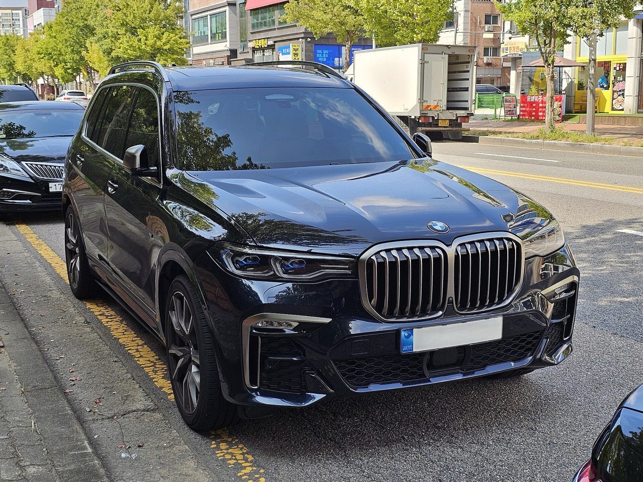 A black BMW X7 M50i SUV parked at a curb, front three-quarter view showing its large kidney grille.