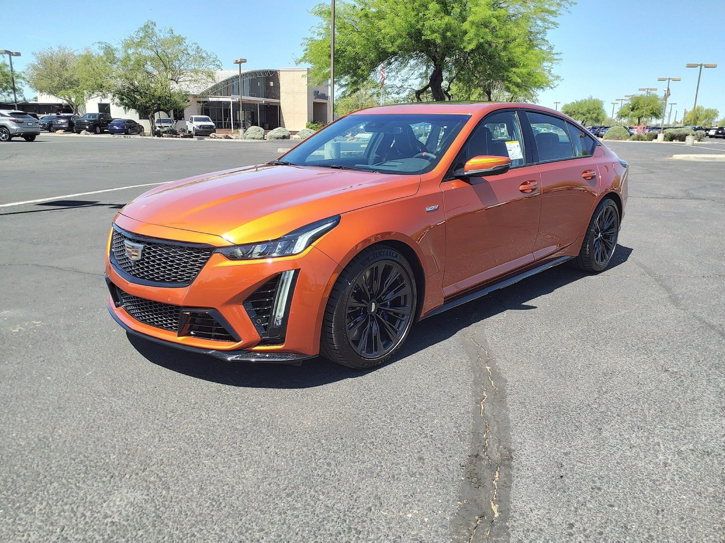 Orange Cadillac CT5-V Blackwing sedan with black wheels parked in a sunny parking lot, seen from the front three-quarter angle.