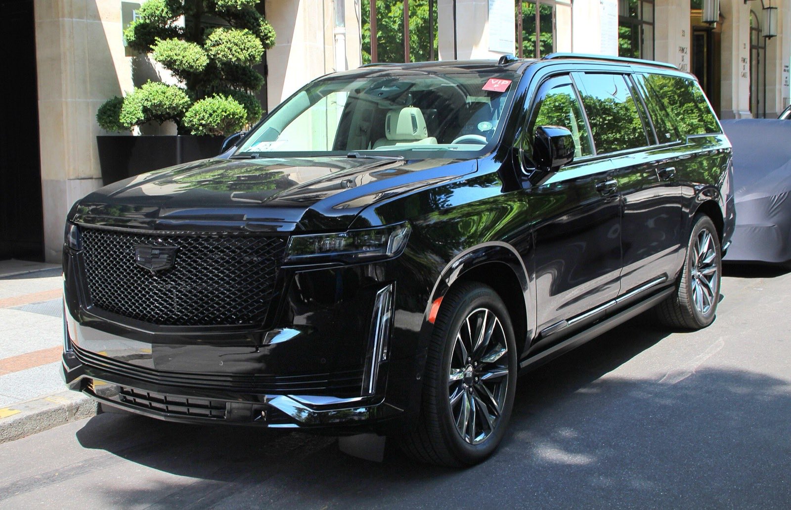 A black Cadillac Escalade ESV parked at the curb of a city street outside a stone building.