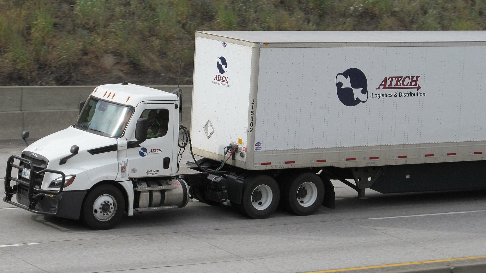 White Freightliner Cascadia day-cab truck pulling a white box trailer along a concrete interstate highway.