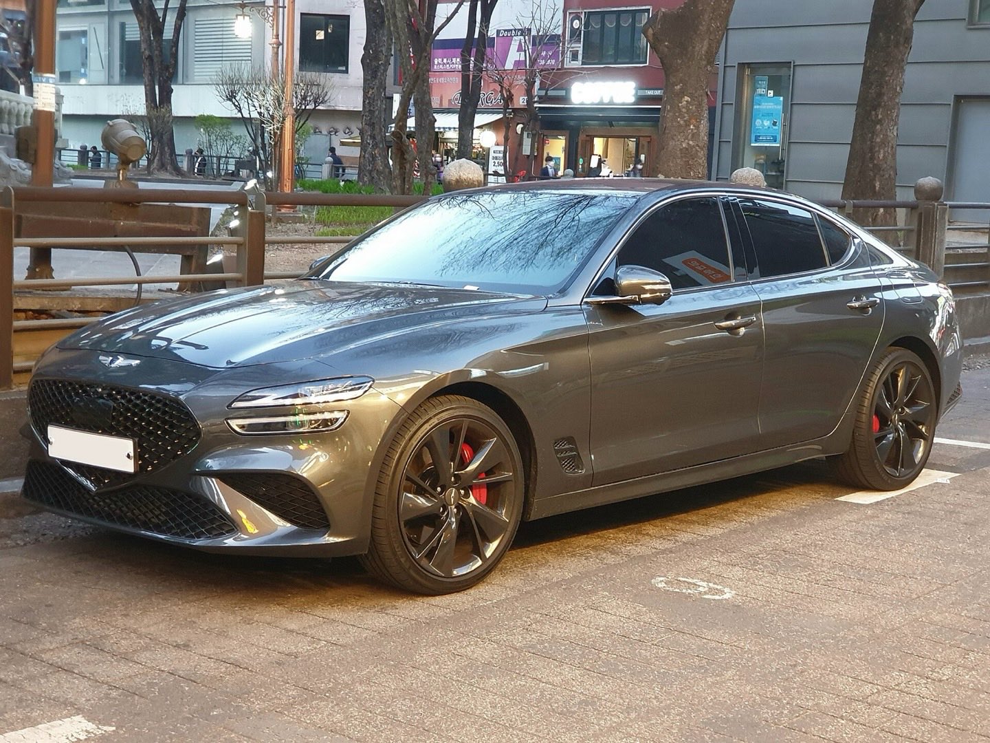 Dark gray Genesis G70 sedan with black wheels and red brake calipers parked at the curb of a city street.