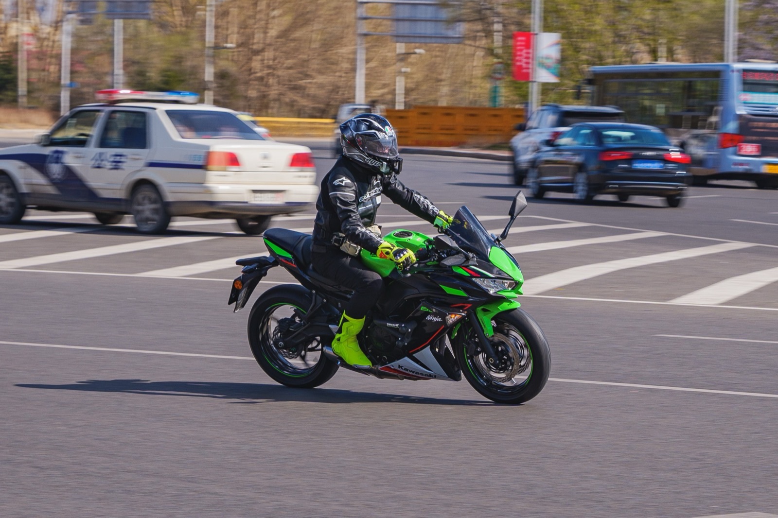 Rider in a full-face helmet, armored jacket, gloves and boots riding a green and black Kawasaki Ninja 650 through a city intersection.
