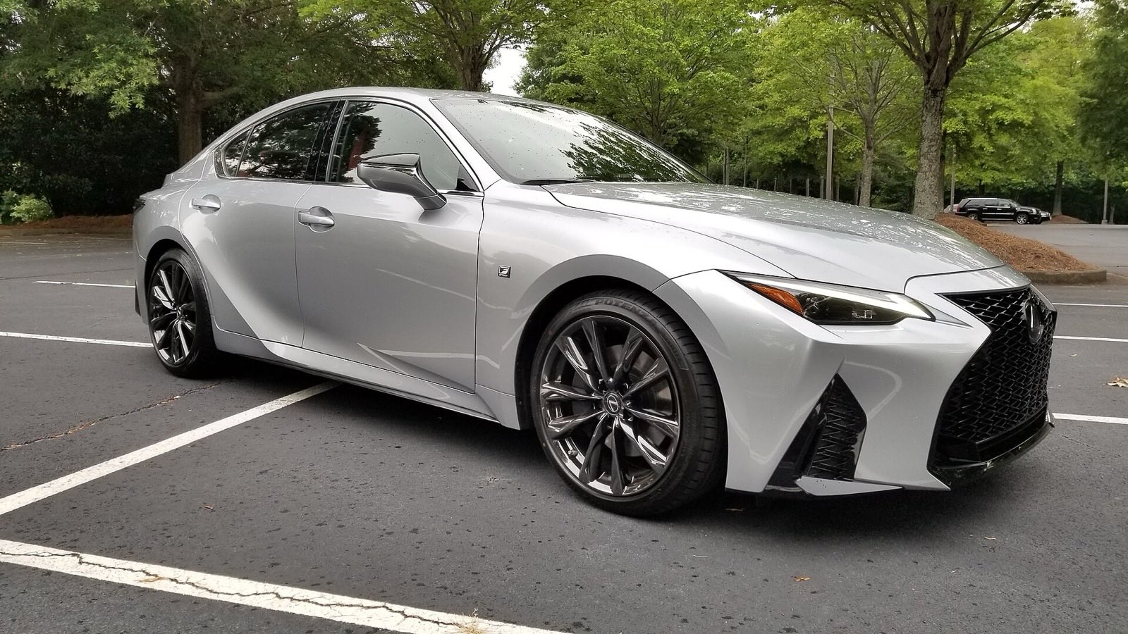 Silver Lexus IS 350 F Sport sedan parked in a tree-lined parking lot, seen from the front three-quarter angle.