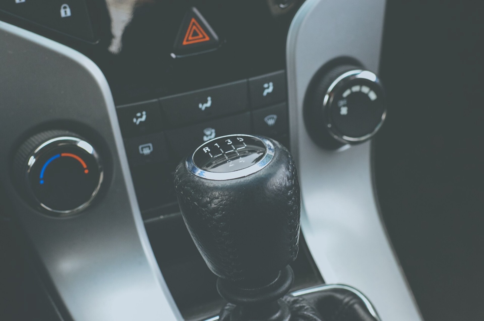 A leather six-speed manual gear knob, with the shift pattern printed on top, in front of a car’s climate controls.