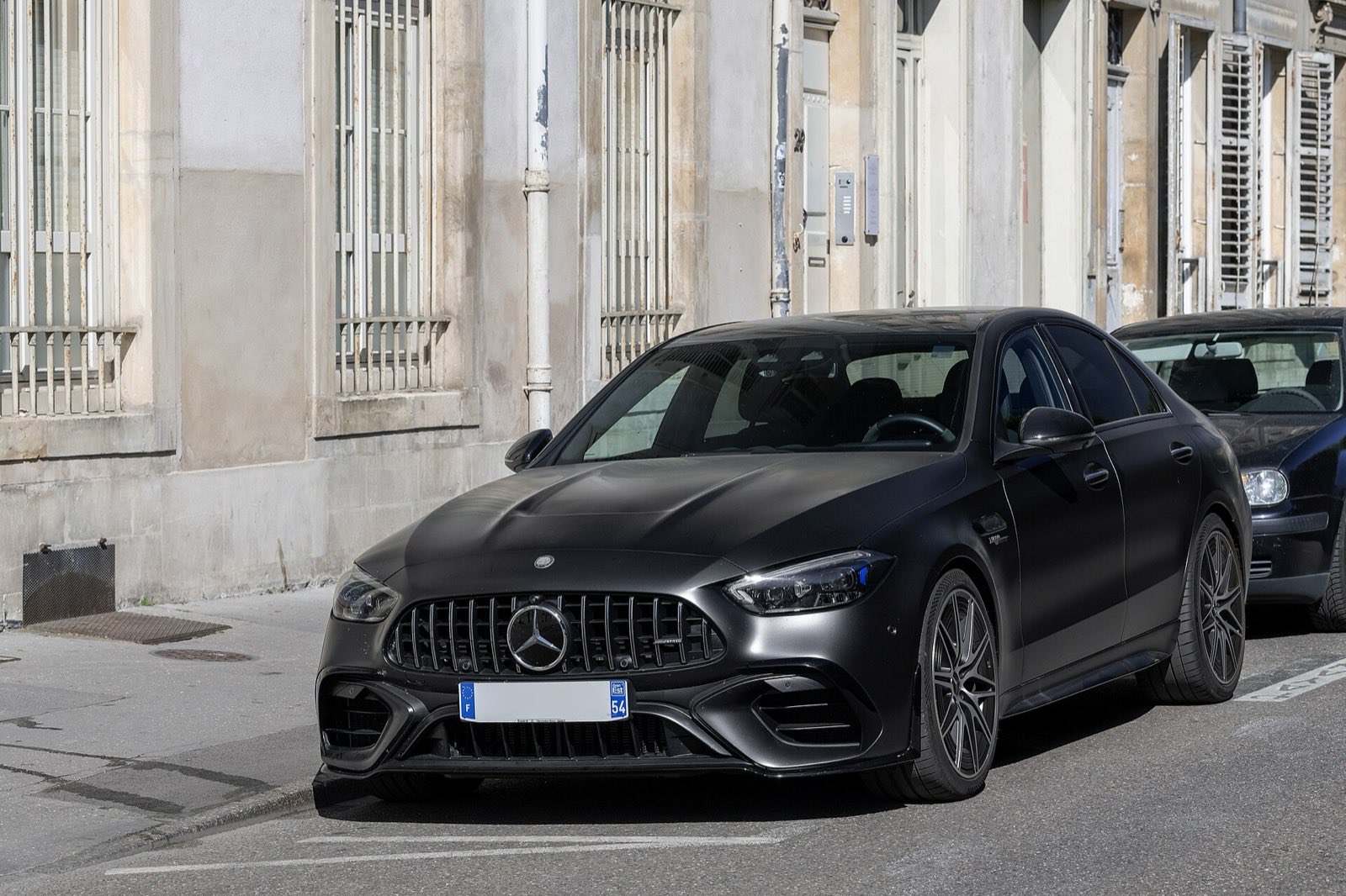 A matte black Mercedes-AMG C 63 S E Performance sedan parked at the curb of a quiet street lined with pale stone buildings.