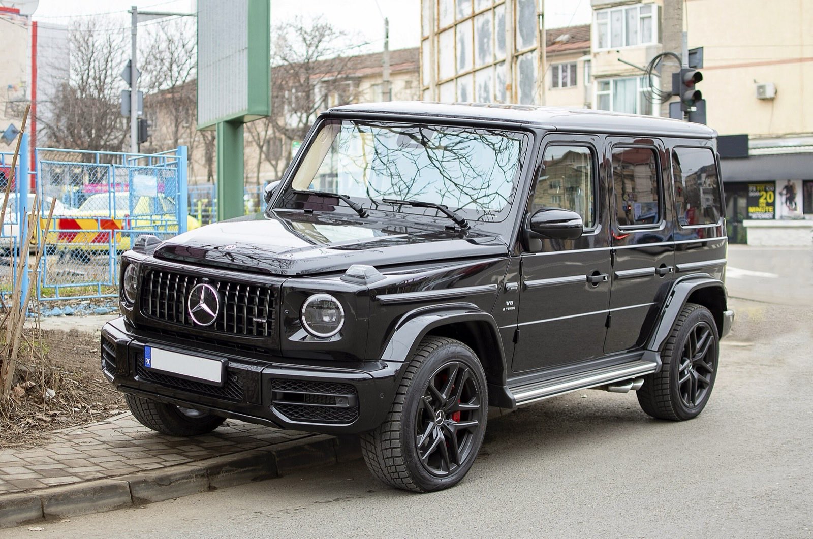 Black Mercedes-AMG G 63 parked at the curb of a city street, seen from the front three-quarter angle.