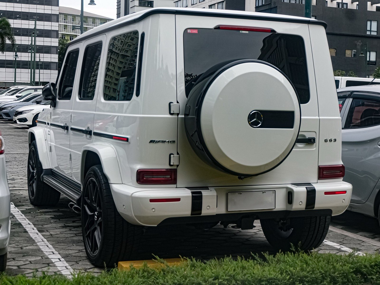 A white Mercedes-AMG G 63 seen from behind in a parking lot, its spare-wheel cover on the side-hinged tailgate.