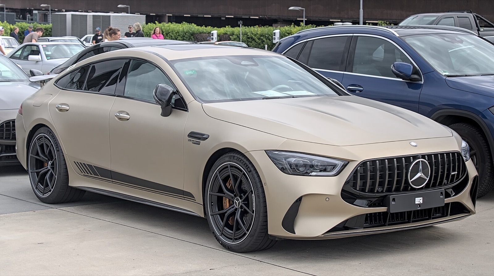 Matte sand-colored Mercedes-AMG GT 63 S E Performance four-door coupe with black wheels and a blank front plate holder, parked on a dealer lot.