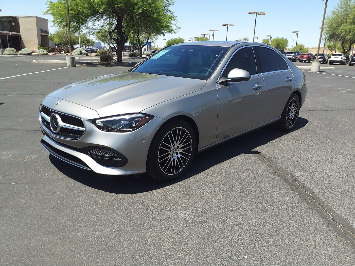 Silver Mercedes-Benz C-Class sedan parked in a sunny, mostly empty parking lot, seen from the front three-quarter angle.